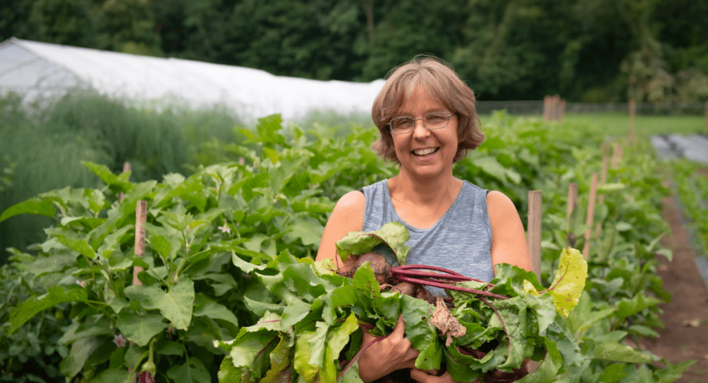 Women in front of farm field holding fresh beets and smiling at the camera.