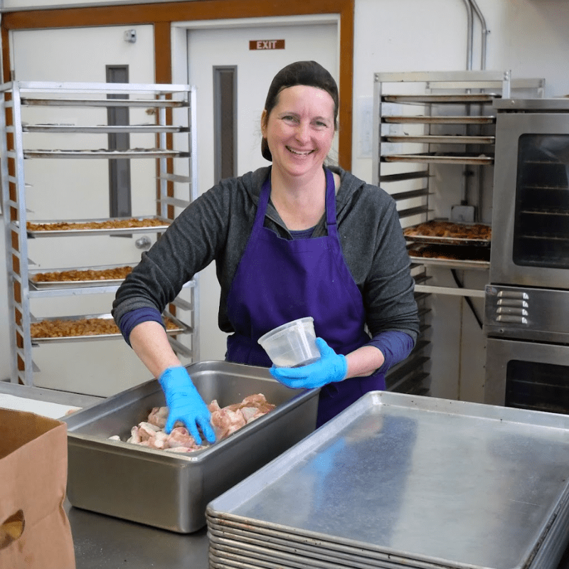 Smiling woman wearing gloves packs food into container.