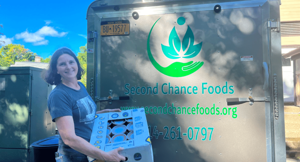 Women holds crate of food in front of the Second Chance Foods cooler