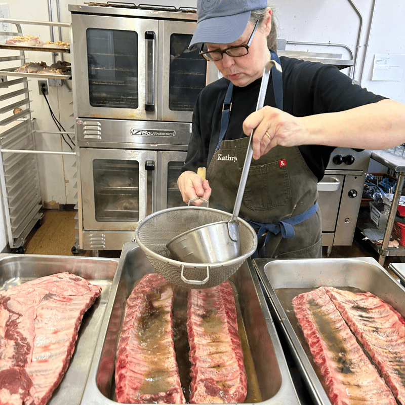 woman pours liquid over pans of raw racks of ribs