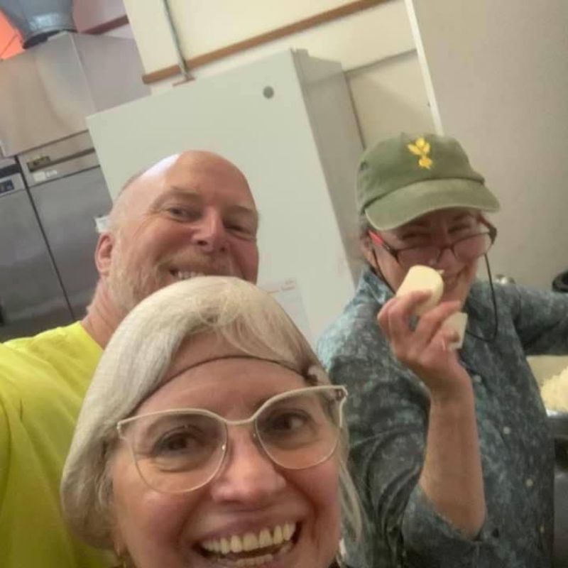 Three smiling people looking at the camera and one holds a peeled potato