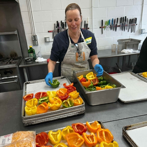Woman in kitchen lays red, green, and yellow bell pepper halves on sheet pans