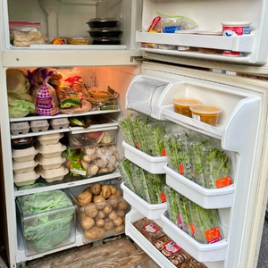 an open community refrigerator stocked with bulk items like eggs, packages asparagus, potatoes, and other groceries for the community