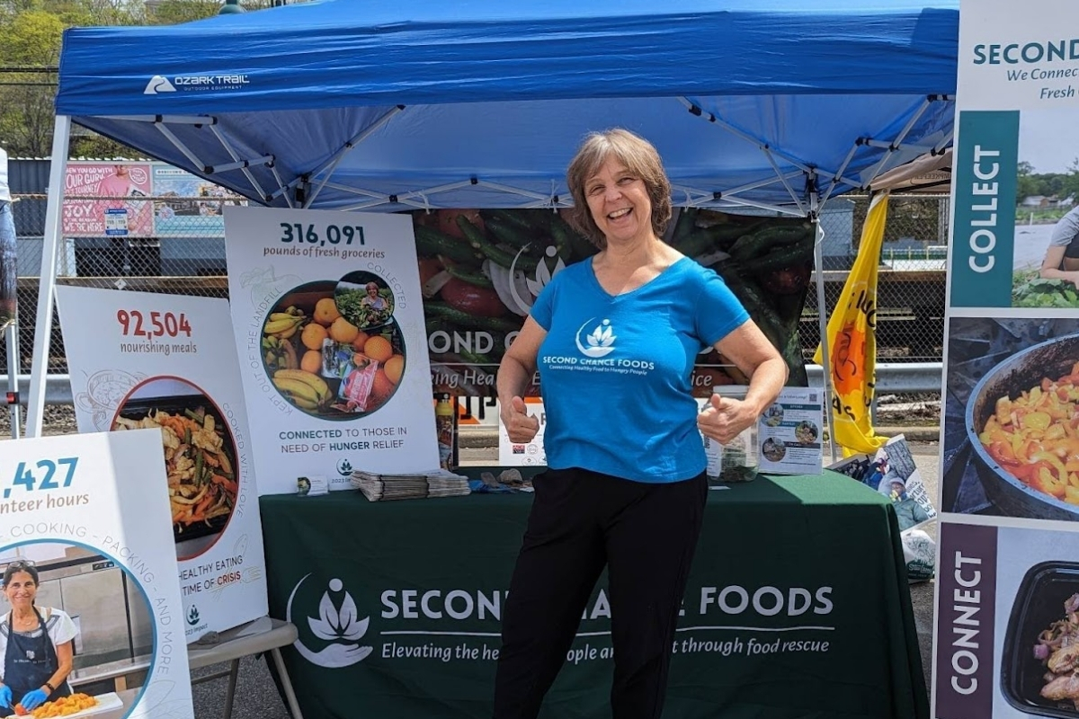 woman stands in Second Chance Foods t-shirt in front of an outdoor booth