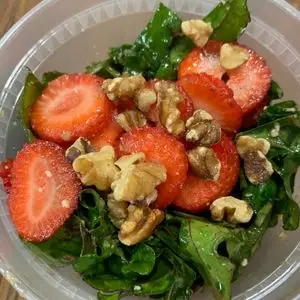 kale and strawberry salad filling a clear to go container