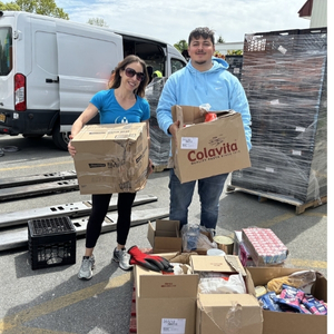 Two people holding boxes filled with food outside of a warehouse