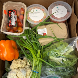 A box filled with prepared meals in quarts and fresh cherry tomatoes, cauliflower head, green onion bunch, orange pepper, half carton of eggs, and other assorted groceries