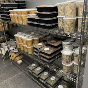 A walk in freezer with a metal shelf filled with large and small containers of prepared meals