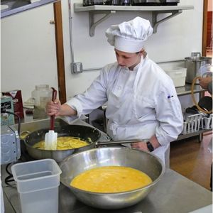 Woman in chef hat and jacket makes eggs over stove