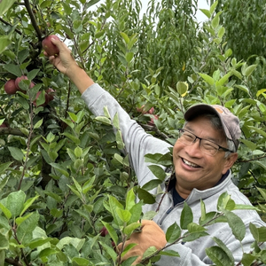 Man surrounded by leaves smiles with arm extended to reach an apple