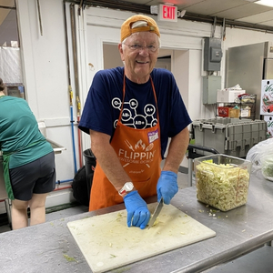 Man in hat and kitchen apron chopping cauliflower.