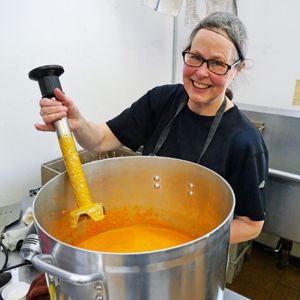 Woman smiles while holding an immersion blender over a pot filled with pureed squash soup