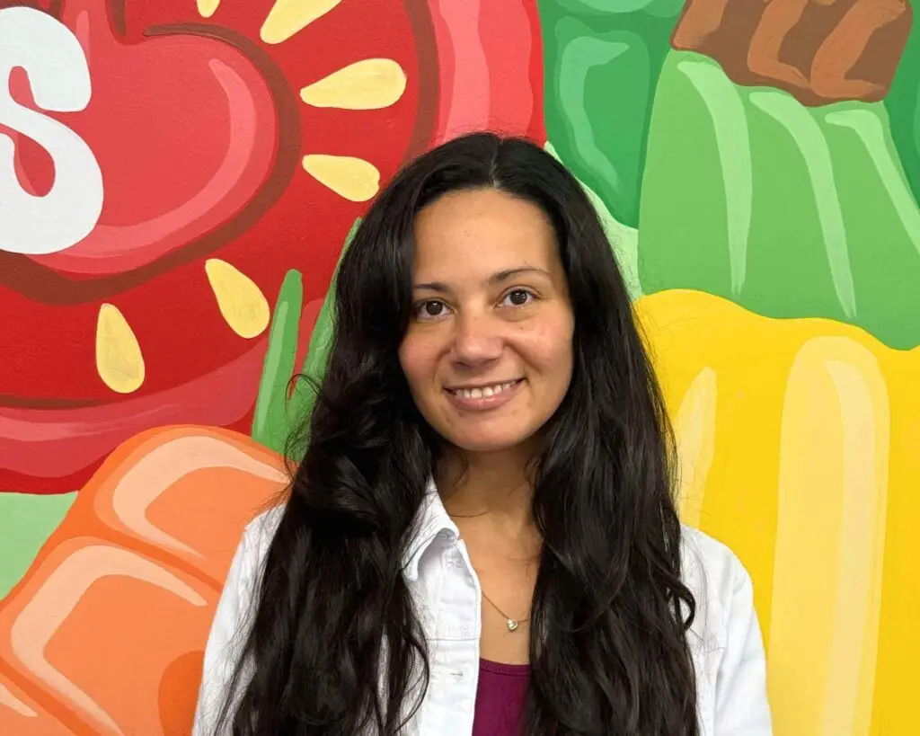 Woman smiles while standing in front of bright mural